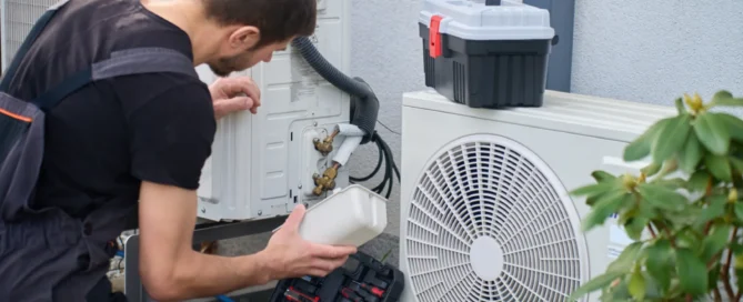 Technician servicing outdoor heat pump unit with tools beside residential house